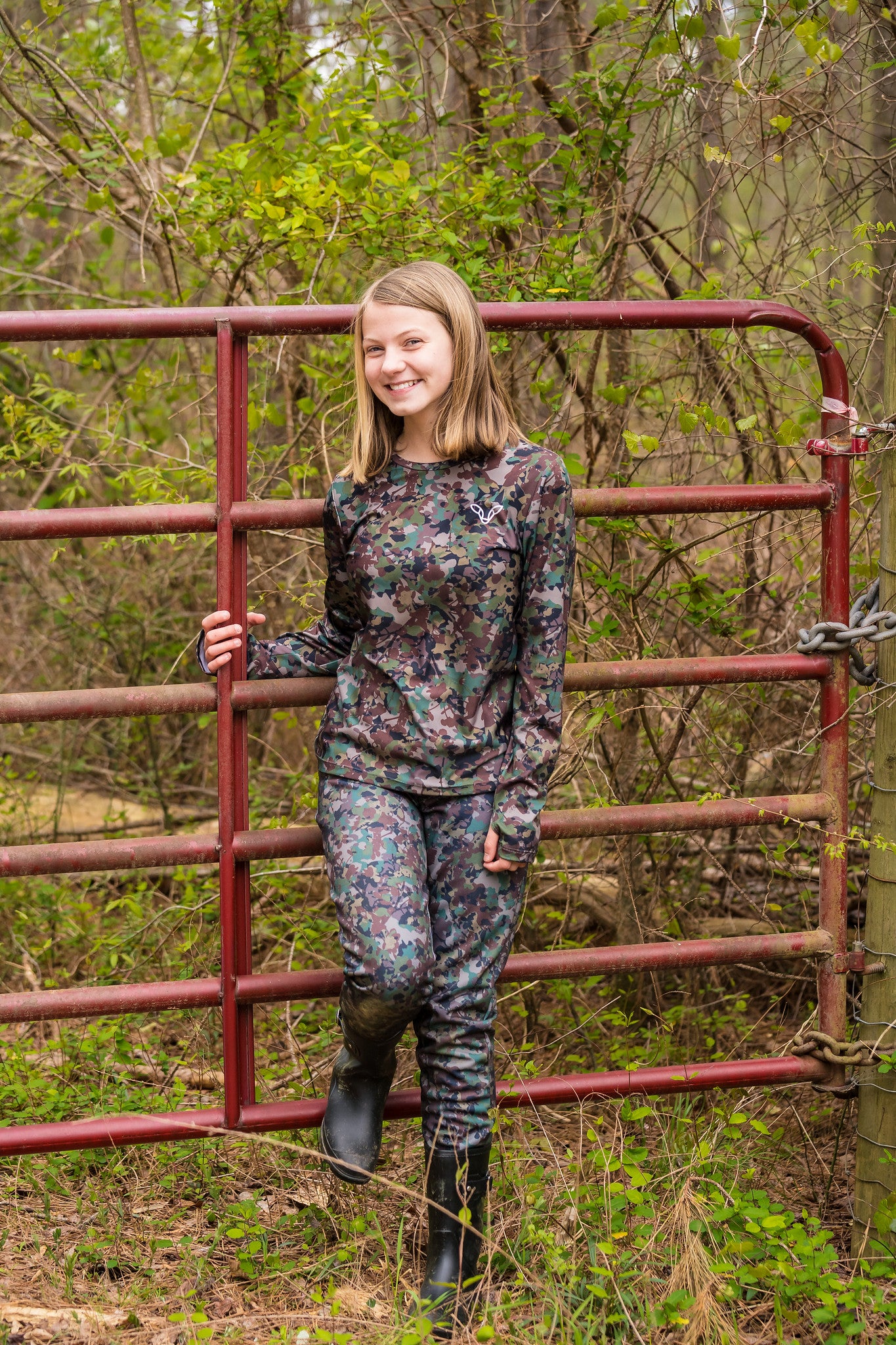 Girl standing by gate wearing camo hunting pants and camo shirt.
