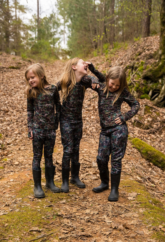 three girls laughing in the woods wearing girls hunting clothes